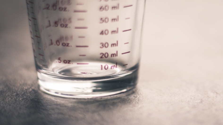 A-cuantas-onzas-equivale-una-taza Parte baja de un vaso medidor transparente en una mesa gris.