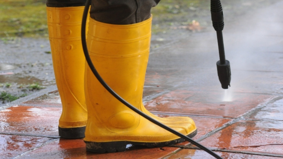 Persona con botas de goma amarillas usando una hidrolavadora en el piso.