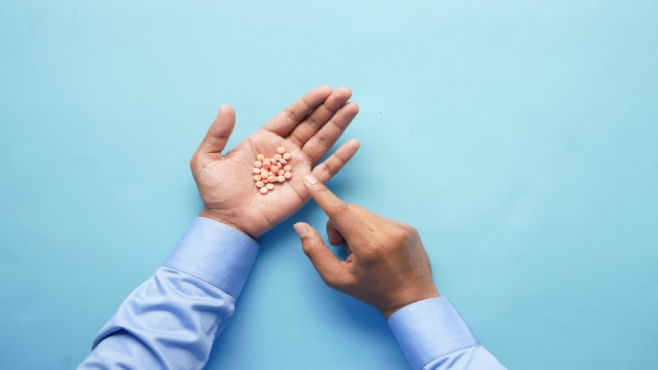 Tiamina-para-que-sirve Hombre con mangas azules con pastillas en una mano señalándolas con la otra mano.