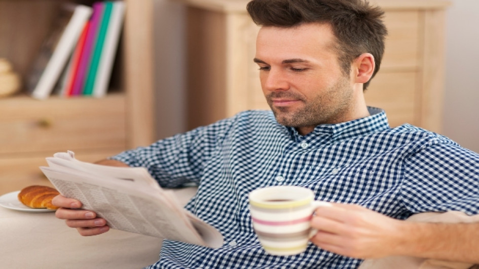 Que-es-un-articulo-de-opinion Hombre sonriente leyendo el periódico con una taza de café.