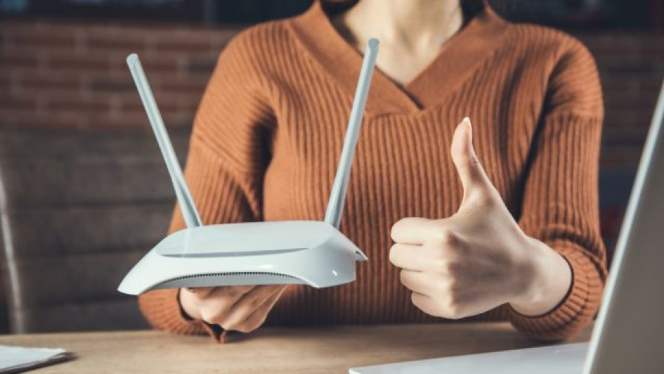 Cómo-proteger-mi-router-de-ataques Mujer sostiene un router y hace el signo de aprobación con la otra mano.