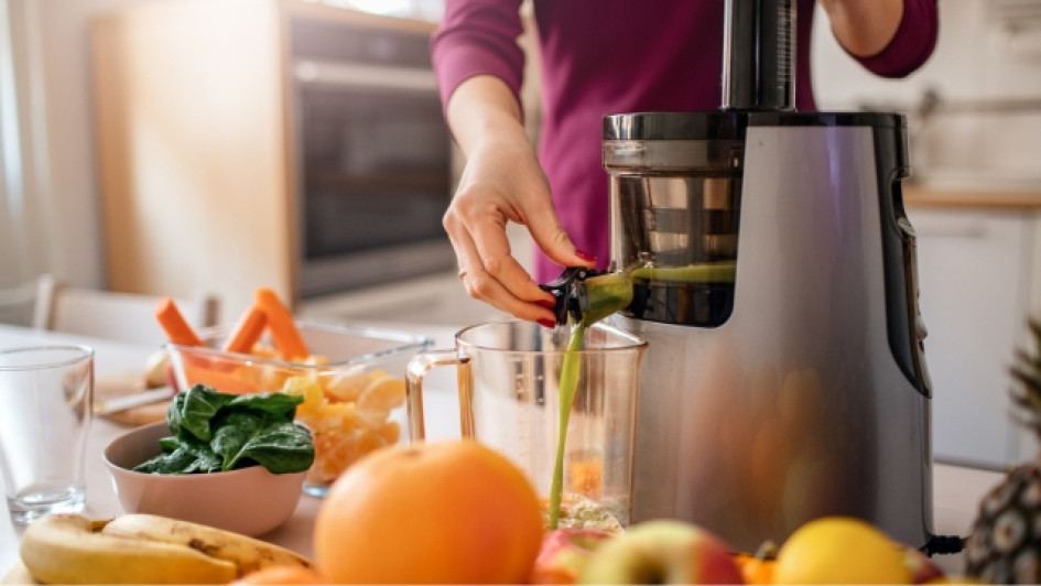 Mujer preparando jugo con muchas frutas y un extractor de jugo en una mesa.