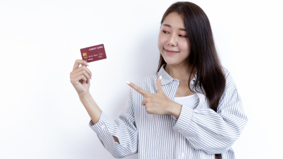 Como-iniciar-vida-crediticia Mujer sostiene una tarjeta de crédito con una mano y la señala con la otra.