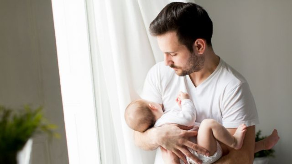 Licencia-de-paternidad-Colombia-quién-paga-cuántos-días-dan-y-cómo-solicitarla Padre cargando a su hijo bebé al lado de una ventana.