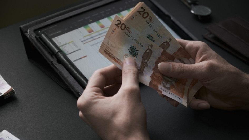 Cuando-se-pagan-los-intereses-de-las-cesantias Dos manos contando billetes de 20 mil pesos colombianos con una tablet en el fondo.
