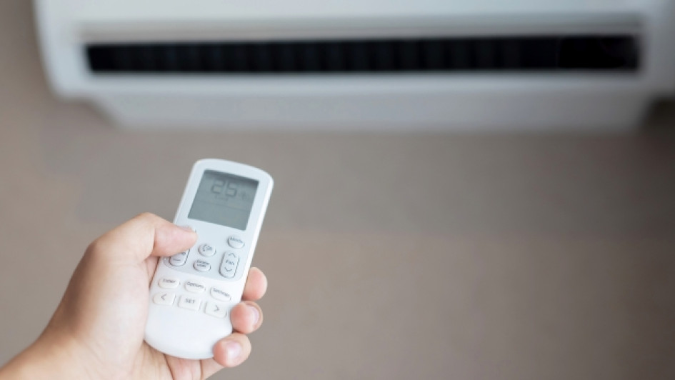 Que-significa-dry-en-el-aire-acondicionado Persona sosteniento un control remoto de aire acondicionado con el aire acondicionado en el fondo.