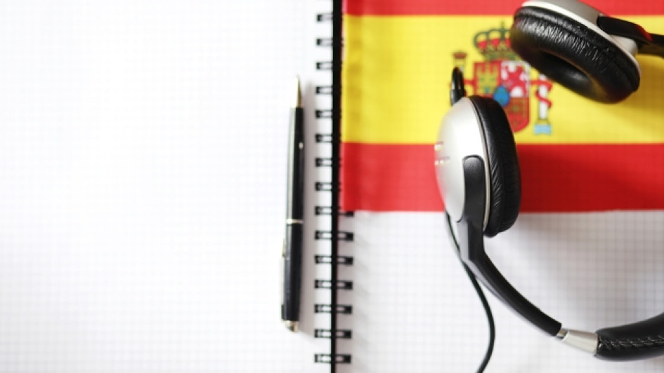 Como-traducir-un-audio-de-ingles-a-espanol Cuaderno con un lapicero, audífonos y una bandera de españa