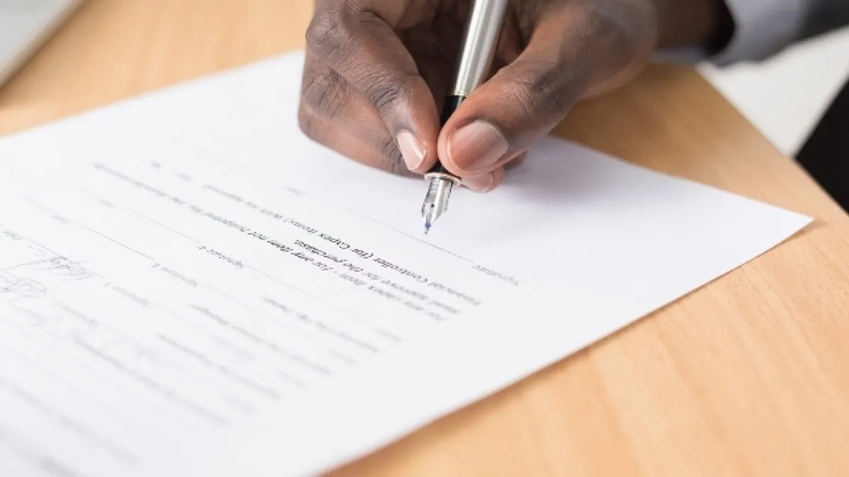 Hombre firma un documento impreso sobre una mesa. 