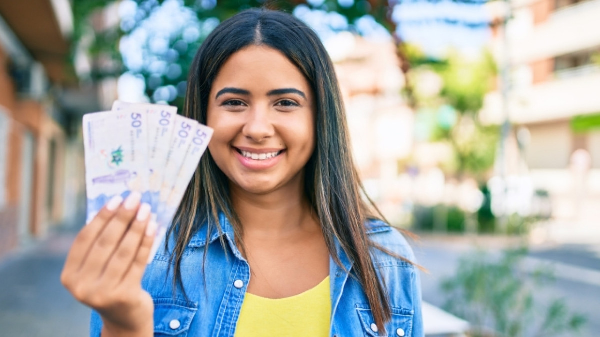Mujer sonriendo mostrando billetes de Colombia en su mano derecha.